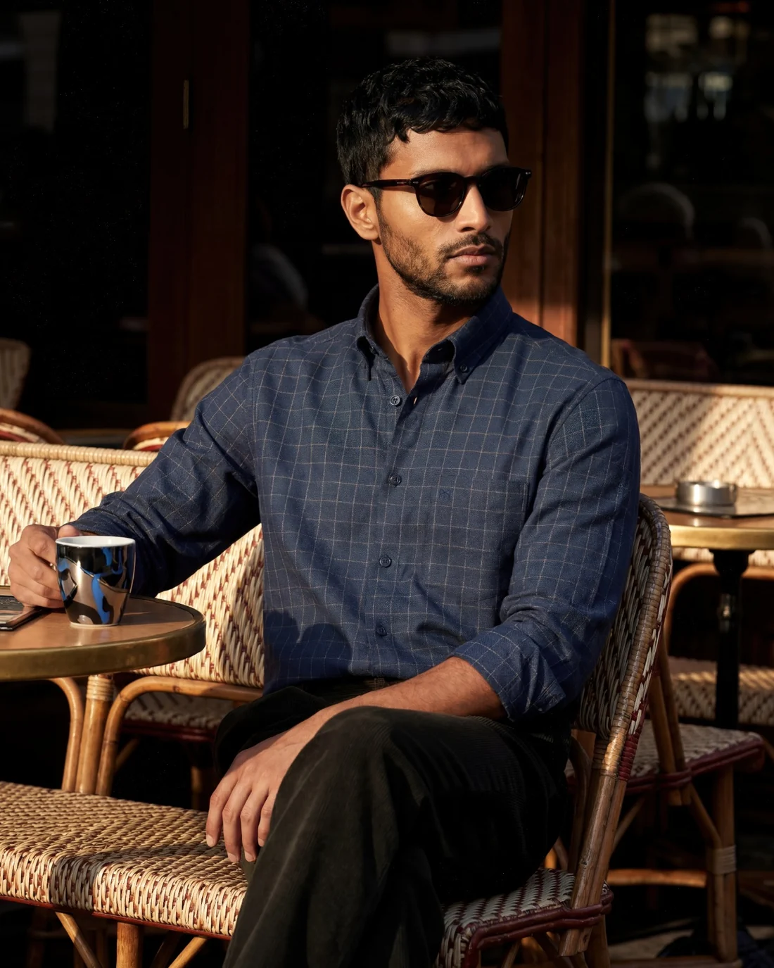 A man in a checked navy shirt seated at a cafe in late afternoon light