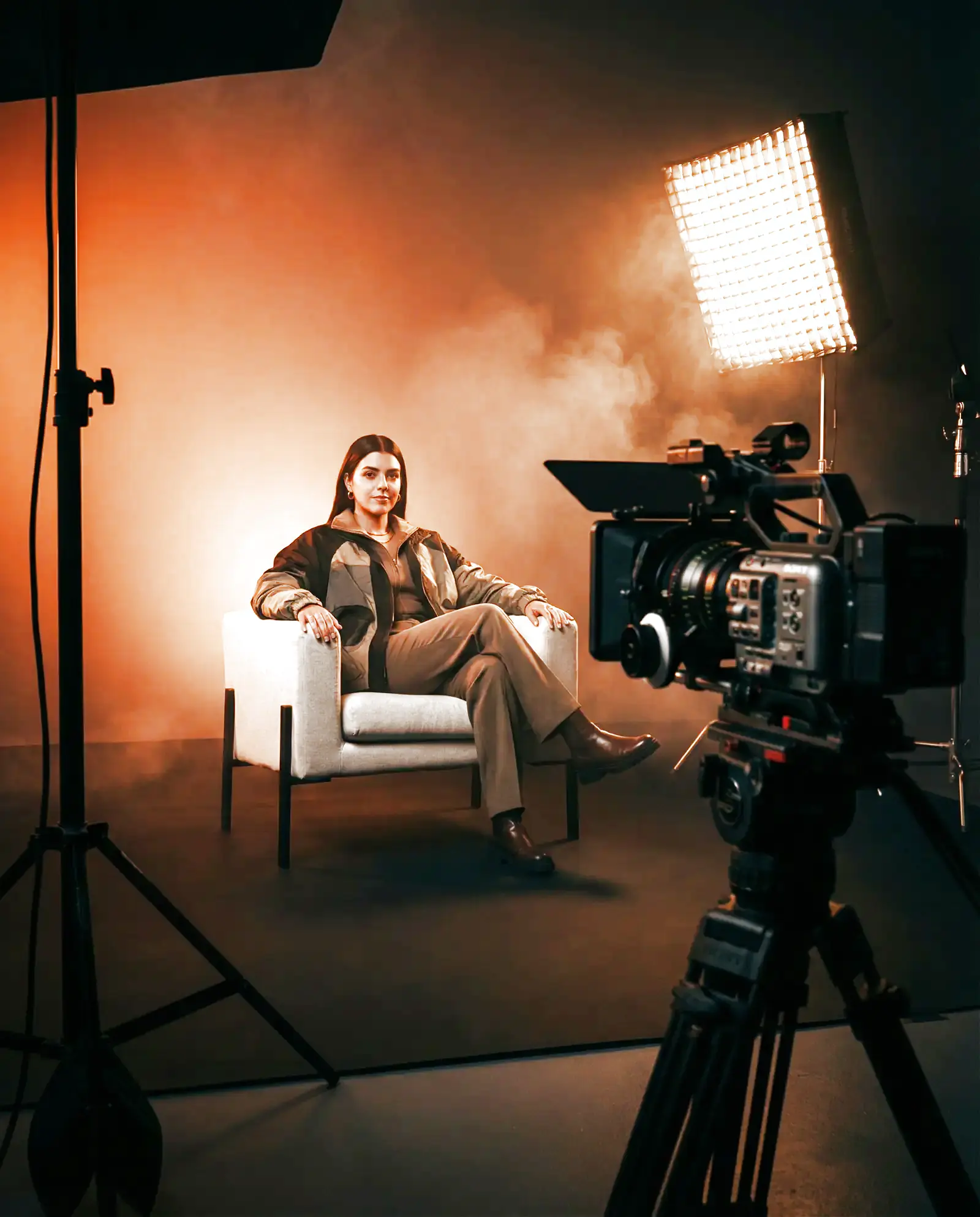 A model seated in a lit studio set with a cinema camera in the foreground